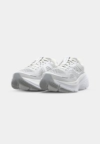 Baskets de sport blanches avec une tige en mesh pour une meilleure respirabilité, semelle rembourrée, semelle extérieure en caoutchouc grise texturée, et accents réfléchissants.