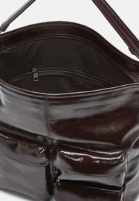Dunkelbraune Lederhandtasche mit offenem Oberteil, das ein Reißverschluss-Innenfach und zwei kleine Fronttaschen mit Klappen zeigt.