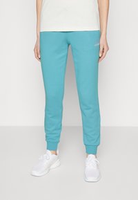 Aqua blue sweatpants with elastic cuffs and waistband, featuring a small white logo on the left side. Paired with white athletic shoes.