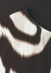 Primer plano de tela con patrón abstracto en tonos marrón y beige con escote redondo sobre un fondo marrón oscuro.