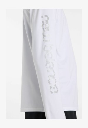 Camicia bianca a maniche lunghe con sottile logo di testo verticale sulla manica, abbinata a pantaloni neri, vista di profilo.