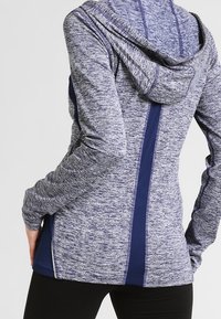 Sudadera deportiva en azul marino y gris jaspeado, con un tejido texturizado, un diseño ajustado y detalles de malla a lo largo de los lados y la parte posterior.