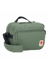 Green fabric bag with a rectangular shape, featuring two zippers on top, a front pocket, a top handle, and an adjustable shoulder strap.