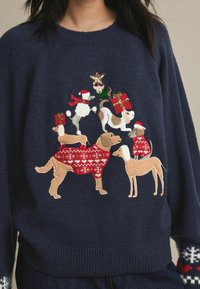 Pull marin orné d'animaux brodés en tenue festive, y compris des chiens en pulls de Noël avec des cadeaux, des accents et une décoration en forme d'étoile.