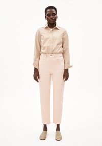 Chemise à boutons beige rayée, pantalon taille haute rose clair et chaussures à enfiler beiges ; tissu lisse et coupe ajustée.