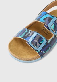 Sandálias de camuflagem azul com duas tiras ajustáveis, apresentando palmilha de cortiça e sola de borracha texturizada, realçadas por fivelas azul claras.