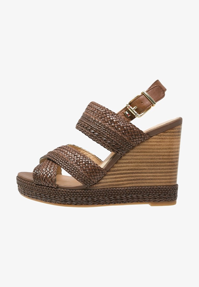 Sandale en cuir tressé marron à talon compensé avec bride de cheville et boucle en doré, présentant une semelle en bois texturé.