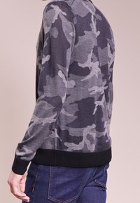 Maglione grigio mimetico a collo rotondo, realizzato in morbido tessuto a maglia, con maniche lunghe e orlo a costine neri.