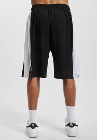 Shorts de sport noirs et blancs en tissu léger, avec une coupe mi-genoux, une taille élastique et des fentes latérales pour la mobilité.