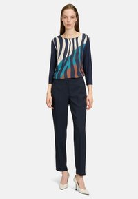 Mörkblå byxor med rak skärning, kombinerade med en flerfärgad topp med ränder och rund halsringning. Slät tygtextur.