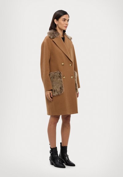 Dunkelbrauner, doppelt-knöpfbarer Wollmantel mit einem Pelzkragen und mit Pelz gefütterten Taschen. Ausgestattet mit goldenen Knöpfen und einer maßgeschneiderten Passform. Schwarze Knöchelstiefel.