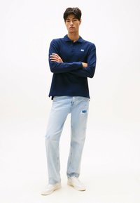 Polo de manga larga azul marino con cuello, combinado con jeans claros desgastados y zapatillas blancas, que presenta un pequeño logo en el pecho.