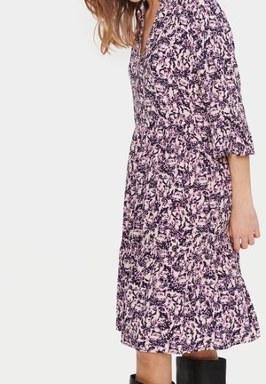 Woman wearing a loose-fitting, pink and black patterned midi dress with three-quarter sleeves and black mid-calf boots, standing sideways.