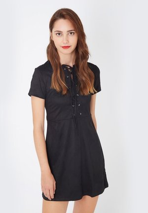 Vestido negro de manga corta con un torso ajustado, detalle de cordones en la parte delantera y falda acampanada. Textura suave, diseño minimalista y longitud a mitad de muslo.