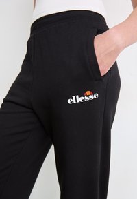 Zwarte katoenen joggers met zijzakken en een elastische tailleband. Bevatten witte "ellesse" branding met gekleurde logoaccenten.