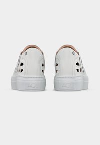 Λευκά δερμάτινα sneakers τύπου slip-on με κομμένα λουλουδένια σχέδια, επίπεδες λαστιχένιες σόλες και ραμμένες λεπτομέρειες, όπως φαίνεται από πίσω.