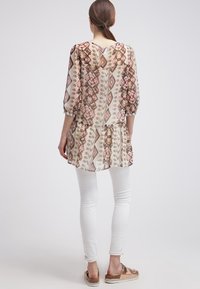 Blusa larga y estampada con dobladillo peplum, que presenta tonos de rosa, marrón y crema. Diseñada con mangas de tres cuartos y un ojal en la parte posterior.