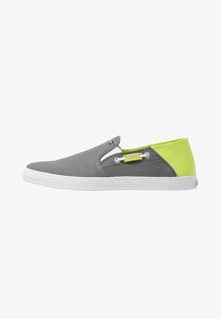 Botte slip-on en toile grise avec une semelle en caoutchouc blanc. Présente une section arrière vert fluo et des détails contrastants en blanc. Équipée d'accents à œillets.