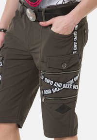 Khaki Cargo-Shorts mit mehreren Reißverschlusstaschen, dekorativem weißen Branding und einem strukturierten schwarzen Gürtel. Strapazierfähiger Stoff mit geradem Schnitt.