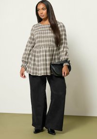 Geruite peplumtop in beige en bruin met elastische mouwen, gecombineerd met wijde zwarte denimbroek en een zwarte clutch. Zachte texturen overal.