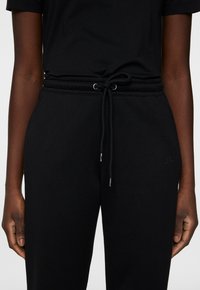 Svarta joggare med elastisk midja, dragsko, sidofickor och diskret logotypdetalj på låret, tillverkade av mjukt bomullsblandat material.