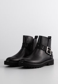 Černé kožené kotníkové boty s hladkým povrchem. S páskem se stříbrnou sponou a robustní podrážkou pro lepší přilnavost.