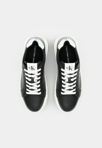 Czarne skórzane sneakersy z białymi gumowymi podeszwami, z białymi sznurowadłami i logo CK na języku. Gładka tekstura i minimalistyczny design.