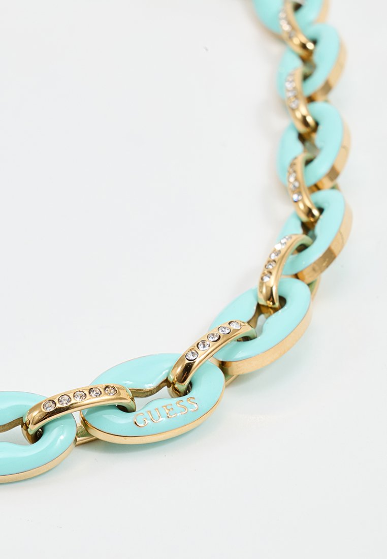 Kette aus goldenen und türkisfarbenen Kettengliedern mit eingefügten klaren Kristallen, wobei ein Glied mit dem Markennamen "GUESS" graviert ist.