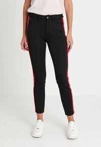 Schwarze Hose im Slim-Fit mit roten Seitenstreifen. Hergestellt aus dehnbarem Material, verfügen sie über einen Knopfverschluss vorne und Gürtelschlaufen.