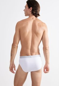 Mutande bianche in cotone con una fascia elastica grigia, viste da dietro. Texture liscia e design classico delle mutande. Nessun motivo o accento.