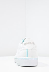 Sneaker in pelle bianca con superficie testurizzata, caratterizzata da accenti azzurri e logo Reebok sul tallone. Suola piatta in gomma.