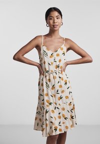 Rochie florală cu un fundal bej, având modele de citrice galbene și frunze verzi. Decolteu în formă de V, bretele subțiri și talie strânsă.