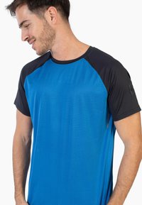 Camiseta atlética azul con mangas raglán cortas negras. Presenta un patrón texturizado a rayas en la parte frontal y un logo en la manga.
