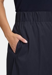 Jupe en tissu bleu marine avec une taille élastique et une poche latérale, présentant une texture lisse et un design simple.