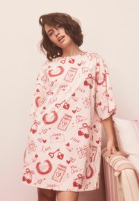 Bomuld natkjole i lyserød med røde tryk af hjerter, hestesko og beskeder som "kærlighed" og "xoxo". Løs pasform, korte ærmer.