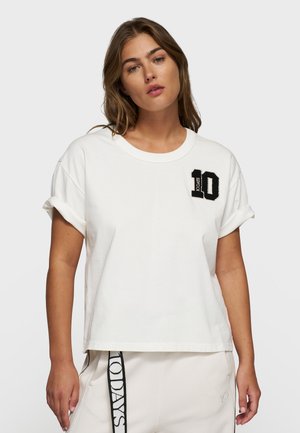 T-shirt bianco a maniche corte con risvolti, con un ricamo nero "10" sul petto sinistro. Materiale in cotone morbido e vestibilità rilassata.
