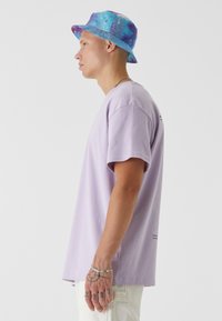 Lilla bomull t-skjorte med korte ermer, supplert med en blå og lilla tie-dye bøttehatt. Enkel design, avslappet passform.