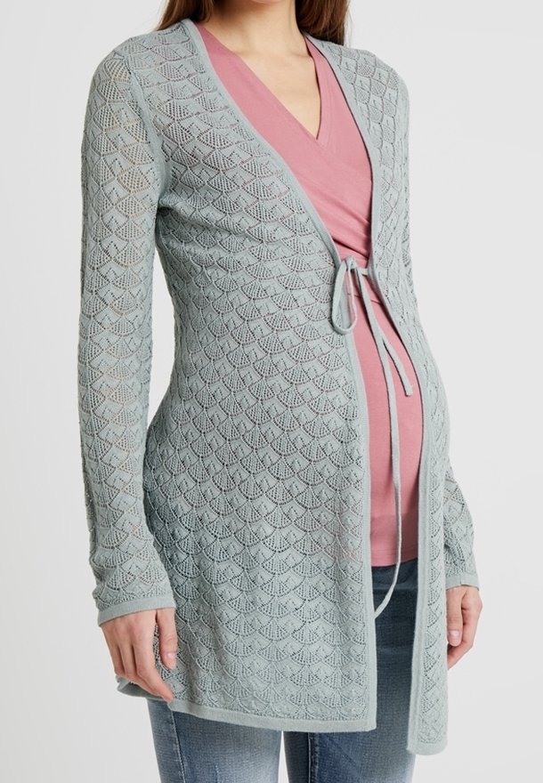 Cardigan en tricot bleu clair avec un motif en diamants, doté d'une fermeture à nouer à la taille et de manches longues, porté sur un haut rose et un jean.