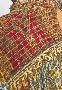 Tissu texturé aux motifs vibrants en rouge, or et bleu ; présente des dessins complexes avec une texture tissée et des accents scintillants.