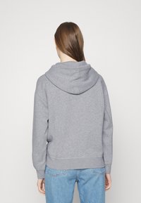 Sudadera con capucha gris de textura suave, corte holgado y puños acanalados. Vista desde atrás, combinada con jeans azules.