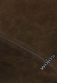 Brązowy zamsz o gładkiej fakturze, z ukośnym szwem i logo "wojas" w kolorze srebrnym.