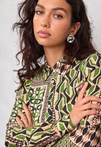 Mehrfarbiges Hemd mit Knopfleiste, das geometrische Muster in Grün, Schwarz und Beige zeigt; mit Kragen und strukturierten Stoffakzenten.