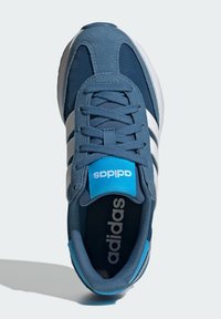 Modré športové topánky vyrobené z semišových a sieťovaných materiálov, s bielymi pruhmi, modrým logom na jazyku a zaobleným dizajnom špičky.