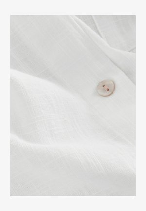 White linen fabric with textured weave, featuring a light pink button detail. Soft, lightweight material. Casual and breathable appearance.