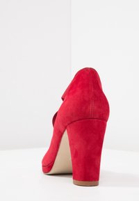Chaussure à talons hauts en daim rouge avec un embout arrondi, une surface texturée et un talon effilé. Dotée d'une sangle arrière pour un soutien supplémentaire.