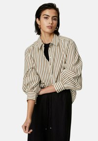 Gestreepte button-up blouse in beige en bruin. Lange, opgezette mouwen; relaxte pasvorm; gedragen over een zwarte top. Gladde textuur met horizontale strepen.
