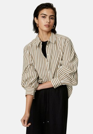 Gestreepte button-up blouse in beige en bruin. Lange, opgezette mouwen; relaxte pasvorm; gedragen over een zwarte top. Gladde textuur met horizontale strepen.