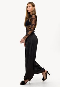 Tenue noire composée d'un top en dentelle transparente avec des motifs floraux et d'un bas en satin. Accessoirisée avec des talons hauts ornés de fourrure noire.