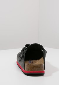 Schwarze Leder-Schlüpfschuhe ohne Rücken mit roter Gummisohle, ausgestattet mit einer Korkeinlage und einem dekorativen Schleifendetail am Riemen.