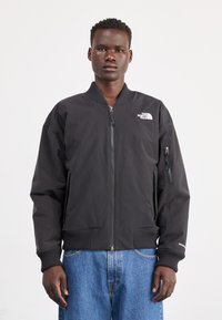 Giacca bomber nera con zip frontale, polsini e fondo a costine, logo sul petto, tasche laterali e tessuto testurizzato. Design leggero e aderente.